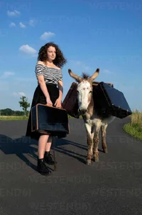 mujer-joven-de-pie-en-un-camino-rural-con-un-burro-cargado-de-equipaje-PSTF00563.webp